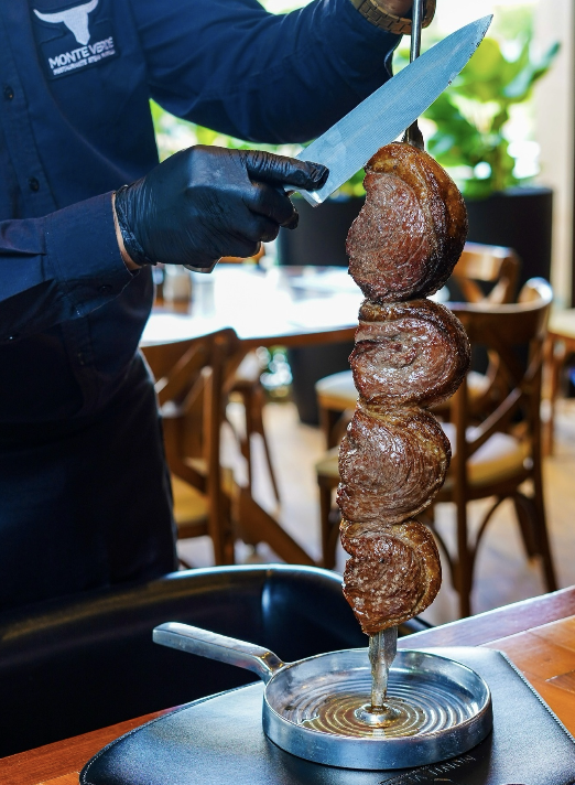 Espeto de picanha sendo fatiado à faca no salão